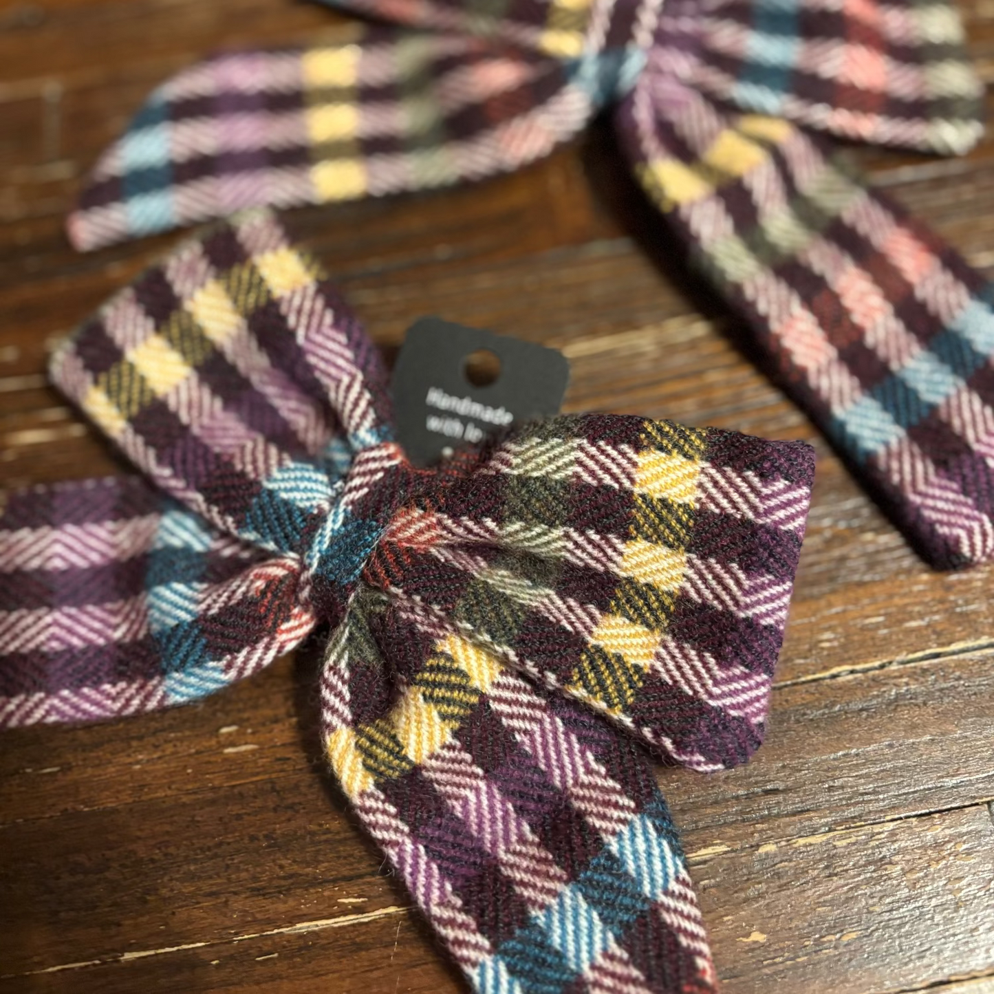 Plaid hair bows on a wooden surface with a visible brand tag.