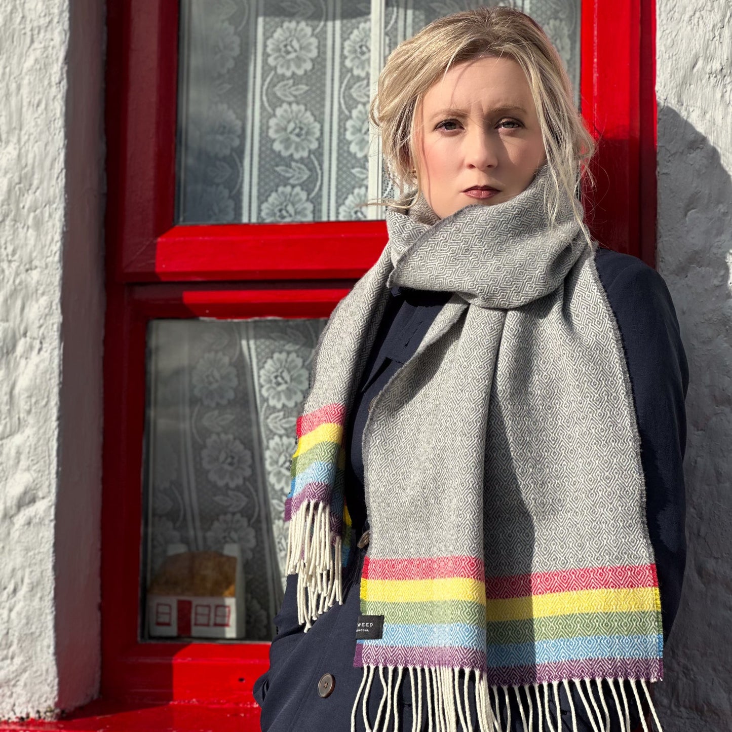Person wearing a gray scarf with colorful stripes in front of a red irish cottage door.