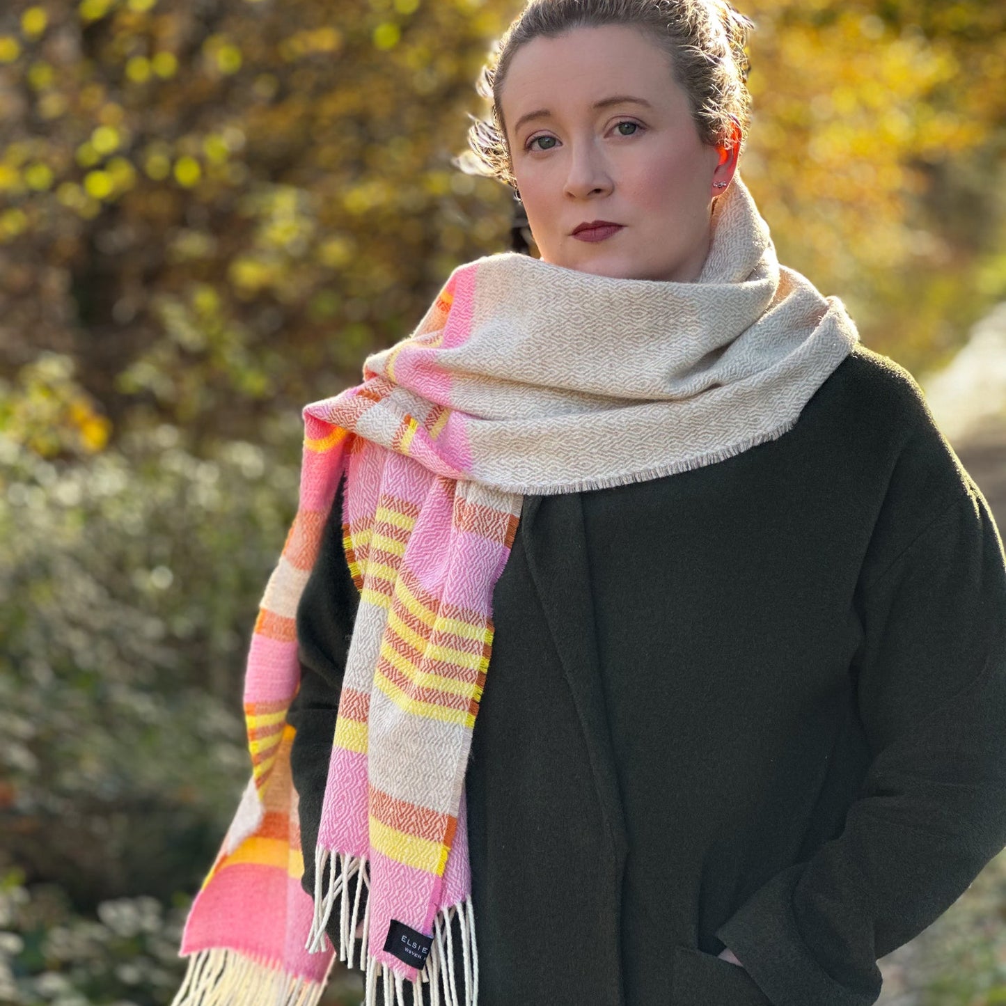 Woman wearing a colorful scarf and dark coat outdoors with trees in the background