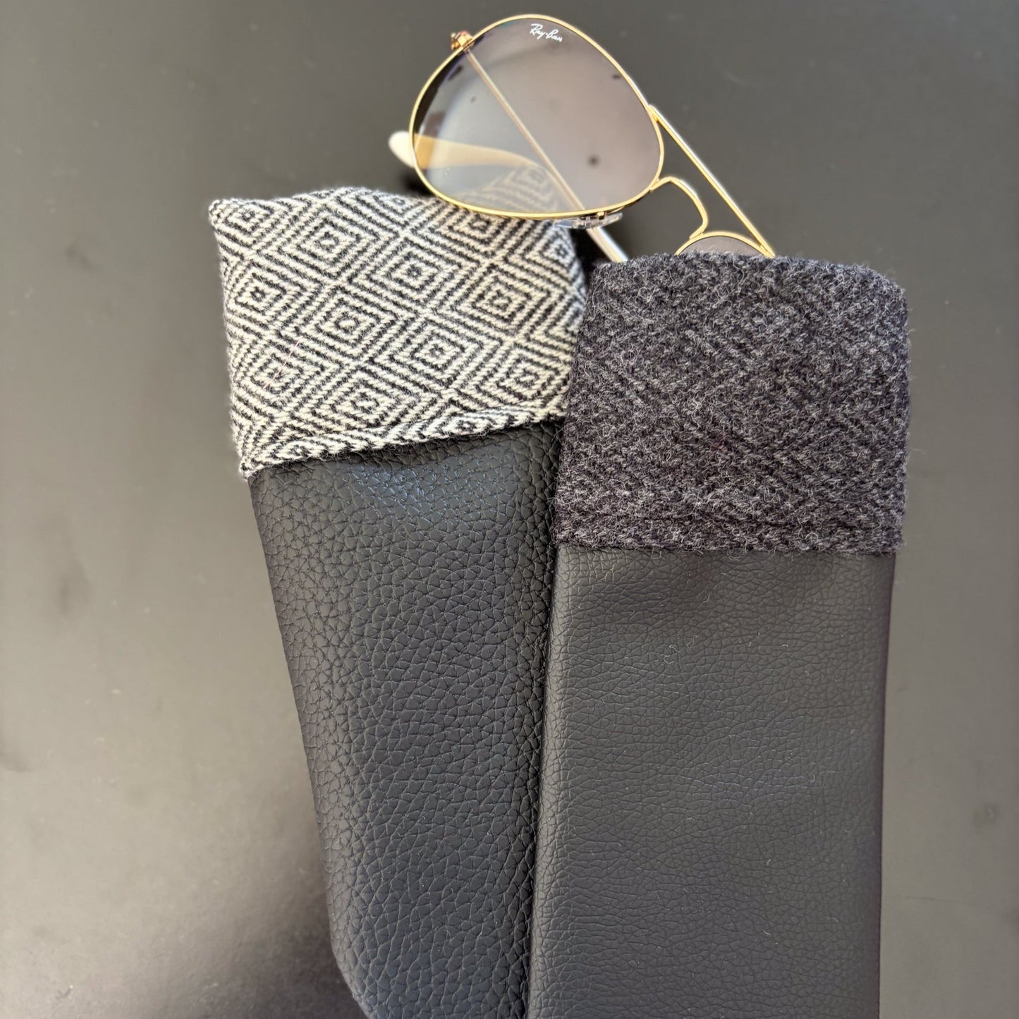 Black leather sunglasses case with patterned flap on a gray background