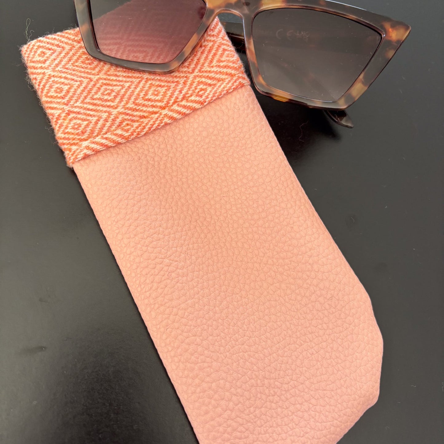 Sunglasses with a tortoiseshell frame on a pink case against a dark background
