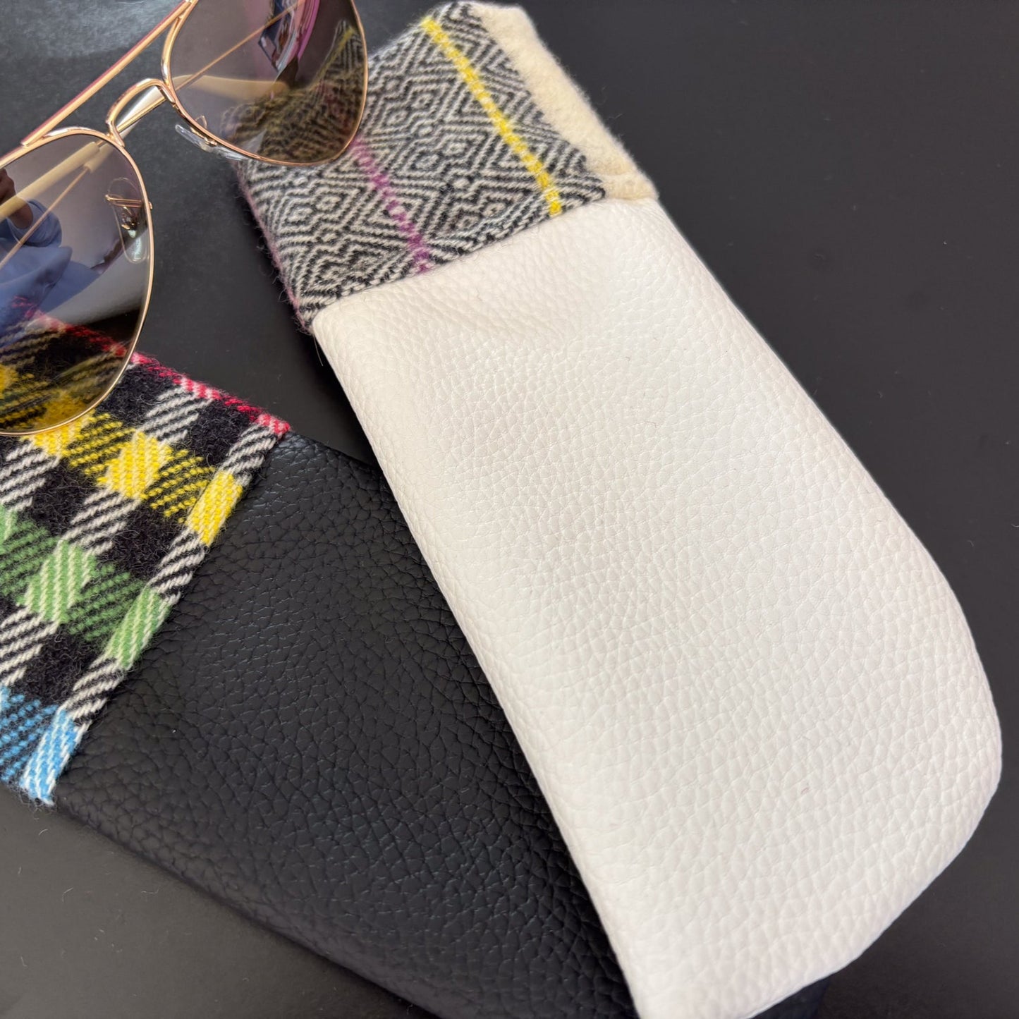 Sunglasses on a patterned case with a white pouch on a black background