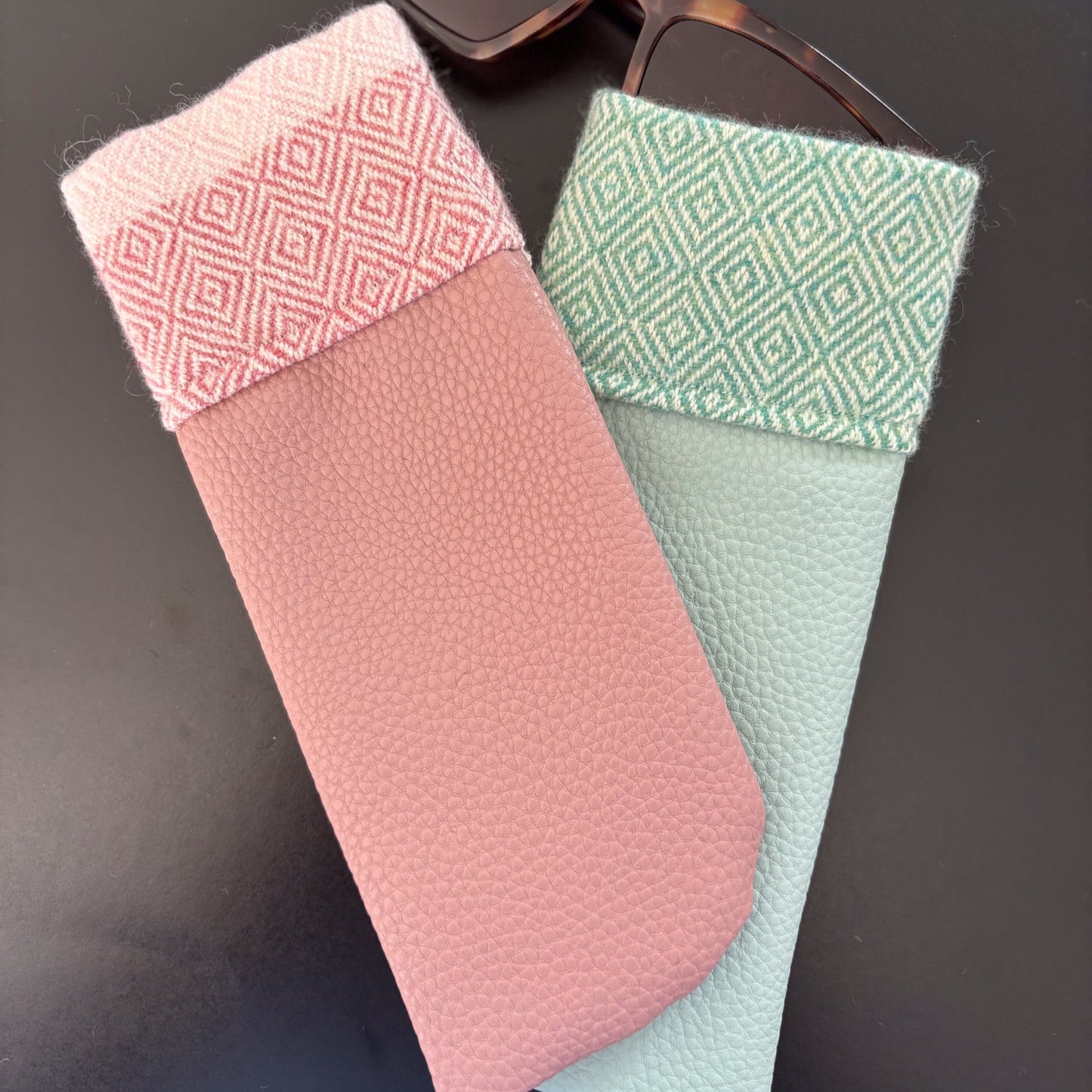 Two textured glasses cases, one pink and one green, with a pair of sunglasses on a dark surface.