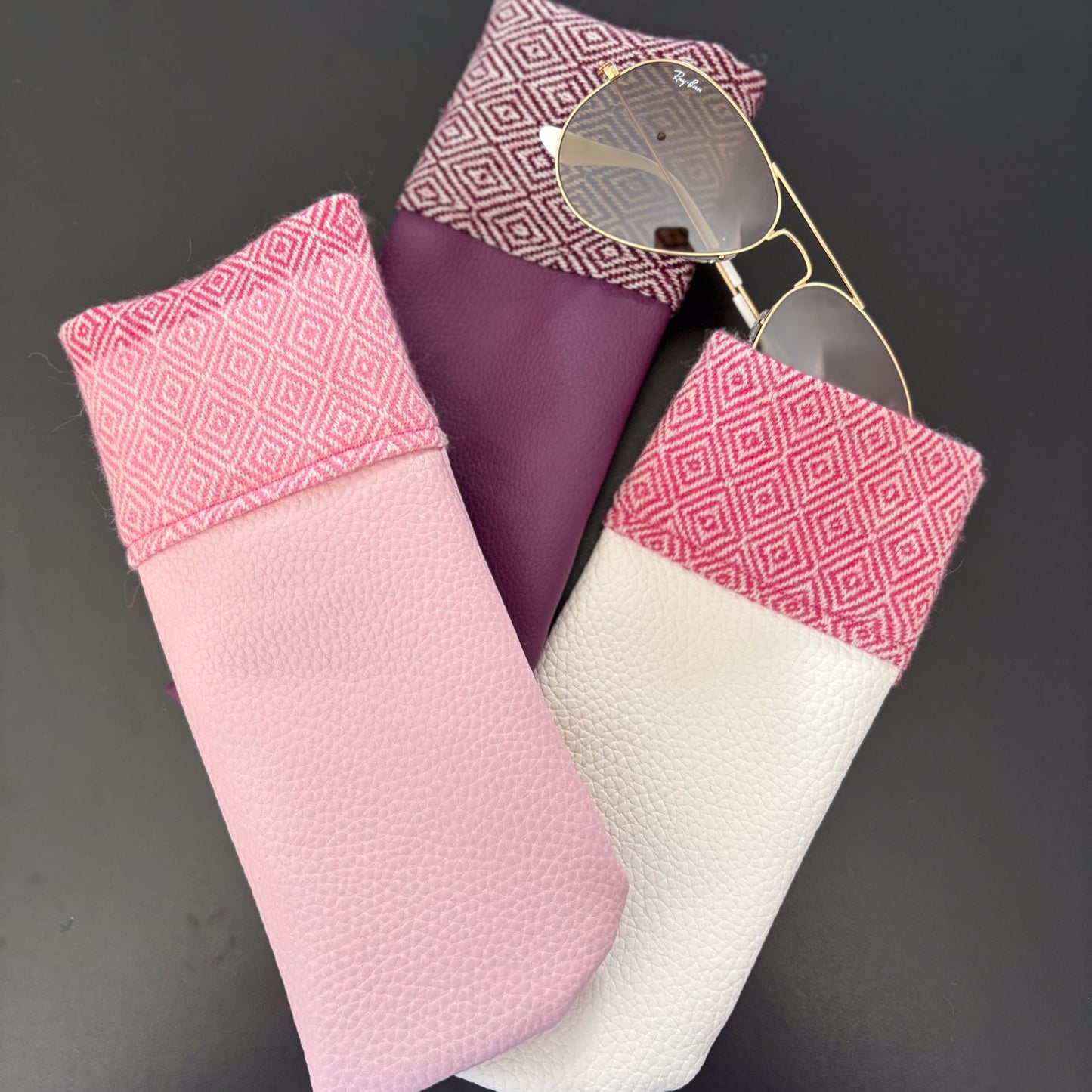 Three colorful fabric cases for sunglasses on a dark surface