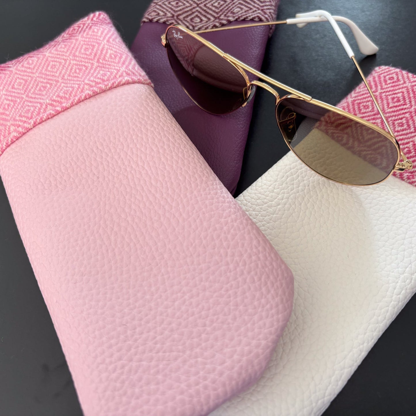 Pink sunglasses case with gold-framed sunglasses on a dark surface