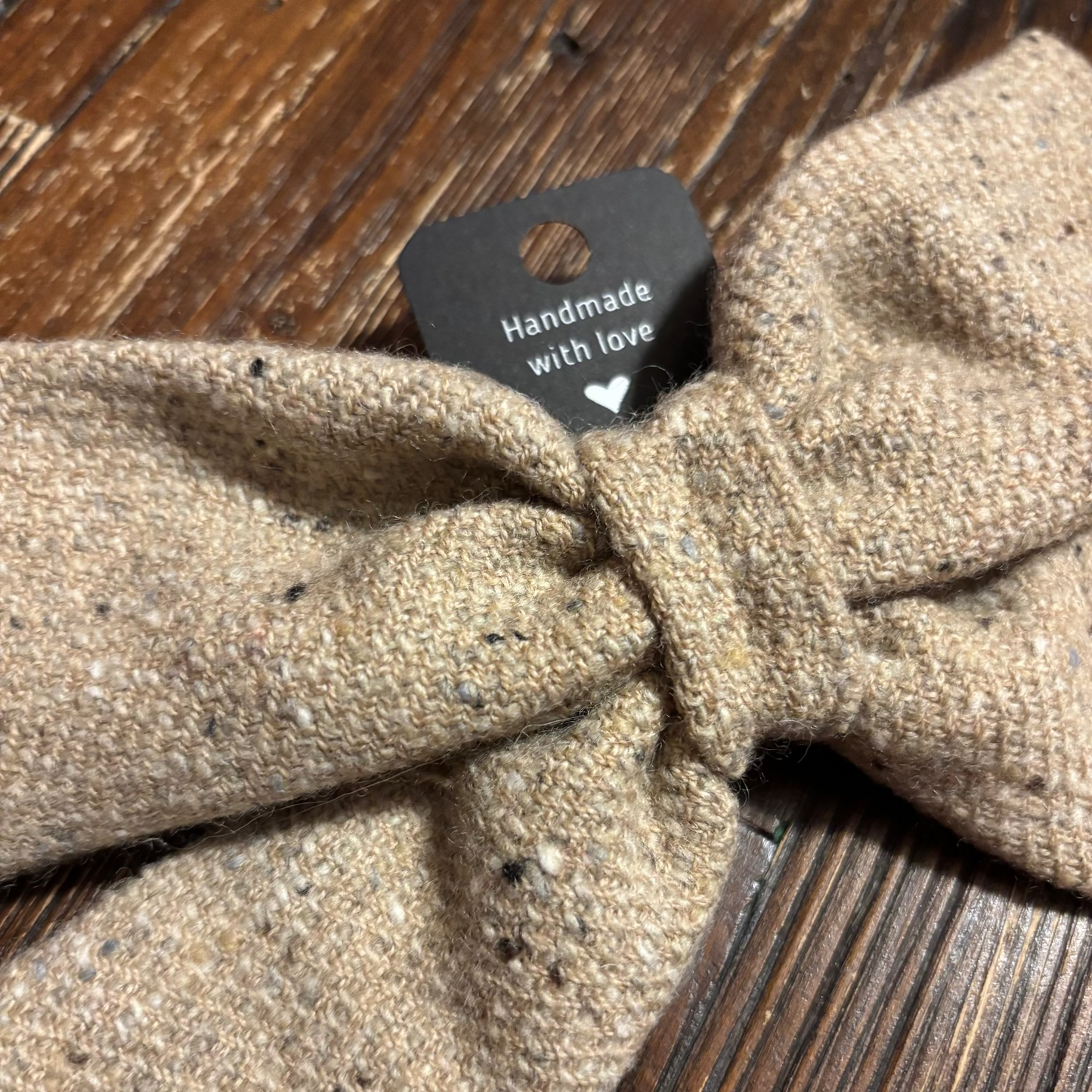 Textured beige bow tie with 'Handmade with love' tag on a wooden surface
