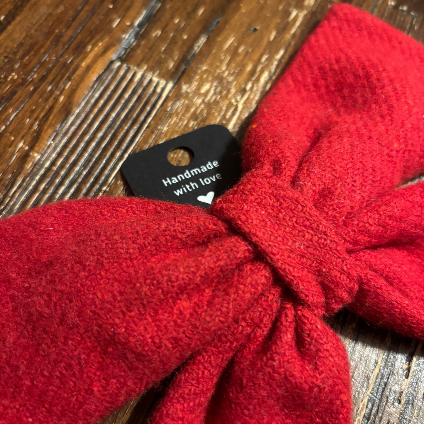 Red knitted tweed hair bow with a 'Handmade with Love' tag on a wooden surface