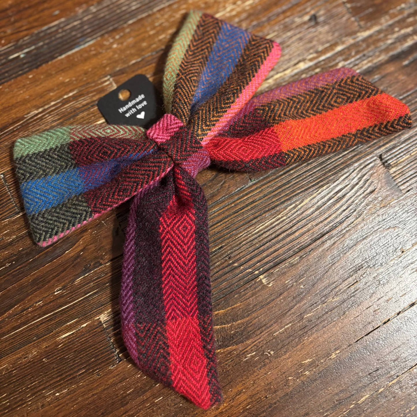 Colorful woven bow on a wooden surface with a visible brand tag.