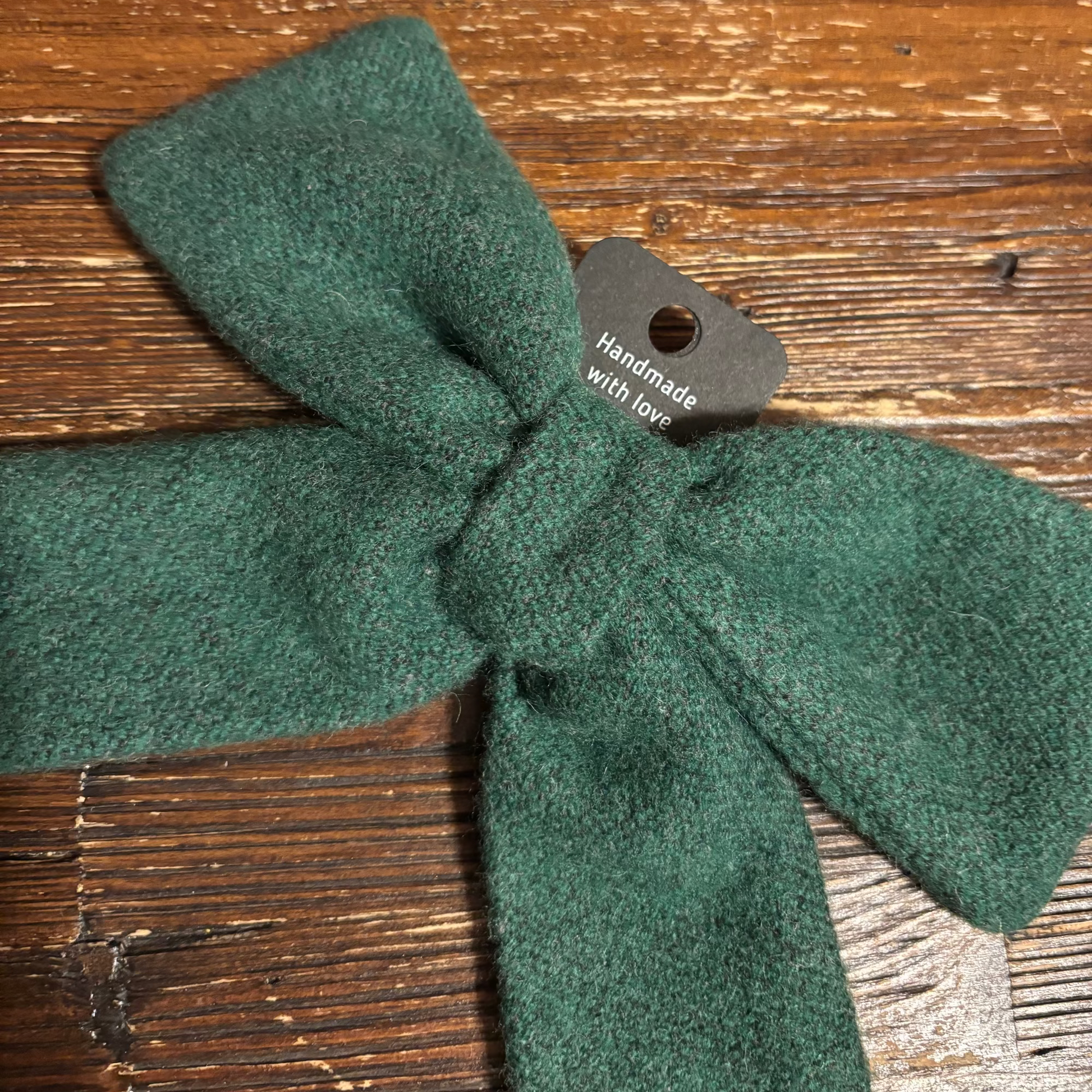 Green knitted bow with a tag on a wooden surface