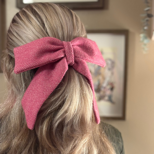 Person with wavy hair wearing a pink hair bow, with a blurred indoor background.