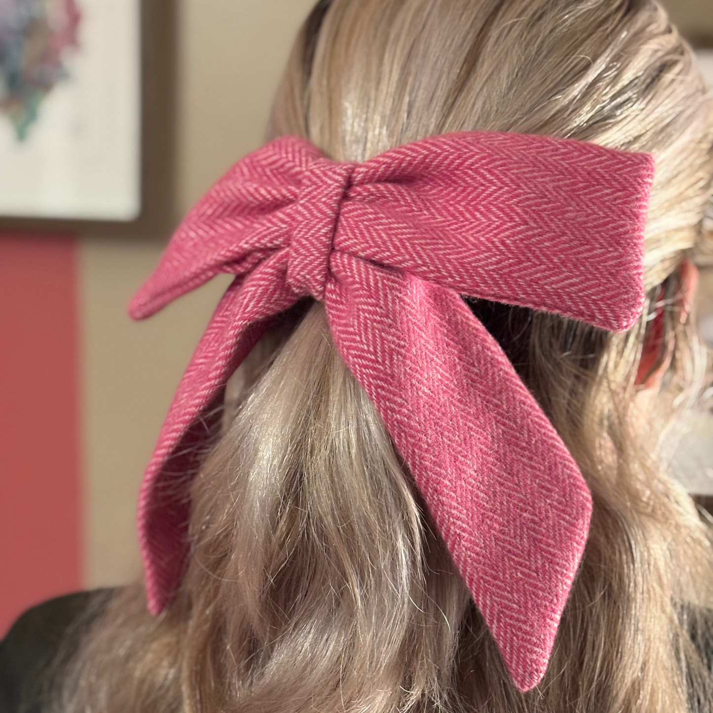 Close-up of a person with a pink bow in their hair, with a blurred indoor background.