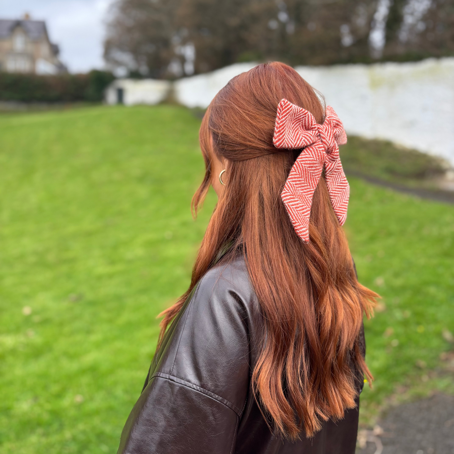 Person with red hair wearing a orange tweed bow outdoors on a grassy area