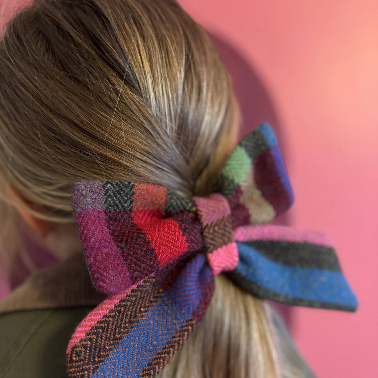 Colorful plaid hair bow in a person's hair against a pink background