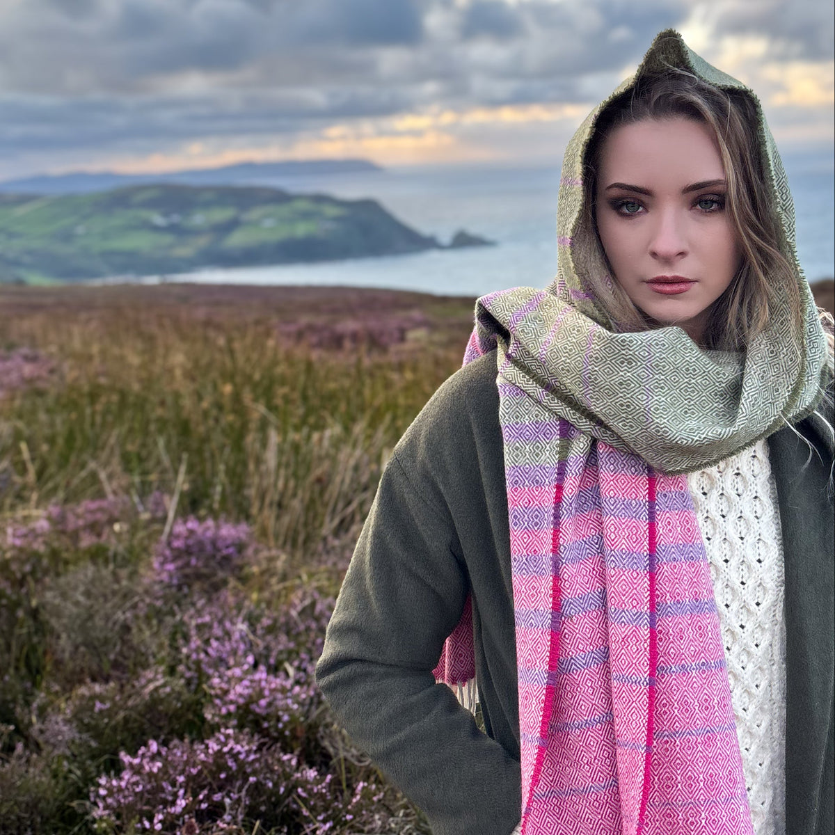 Elsie Tweed oversized scarf being worn as a hood standing on a hill in the heather with a dramatic Irish background 