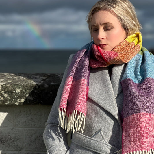 Woman wearing a colorful rainbow inspired scarf with a rainbow in the background