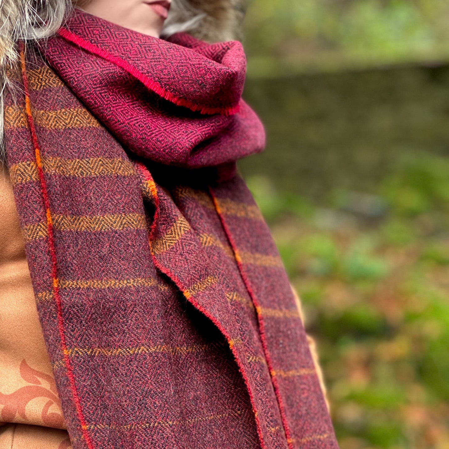 Person wearing a red and orange plaid scarf with a blurred natural background