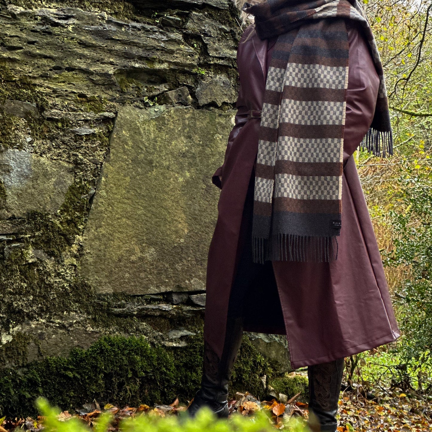 Person wearing a long coat and scarf in a forest setting