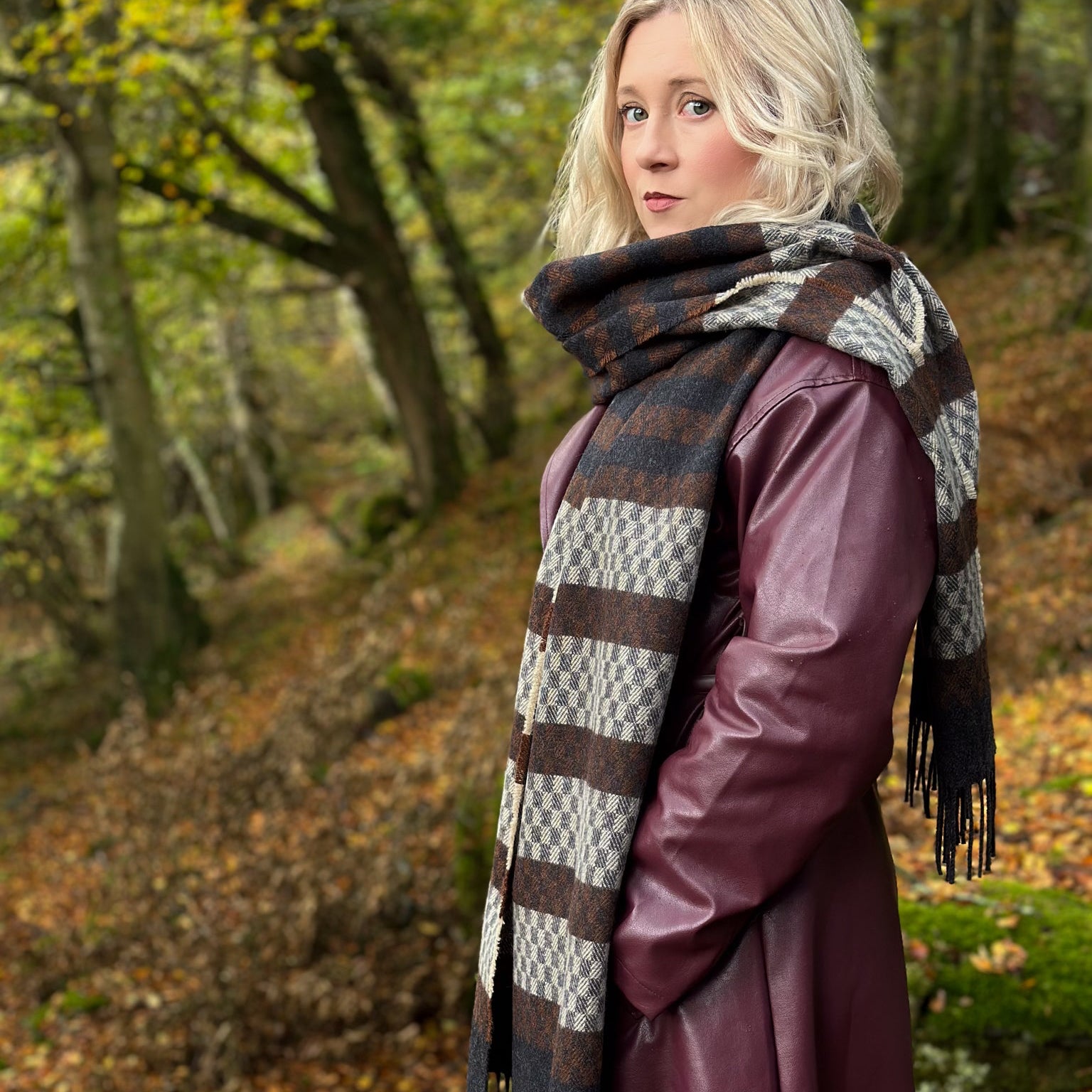 Woman wearing a patterned tweed scarf and plum coat in an autumn forest