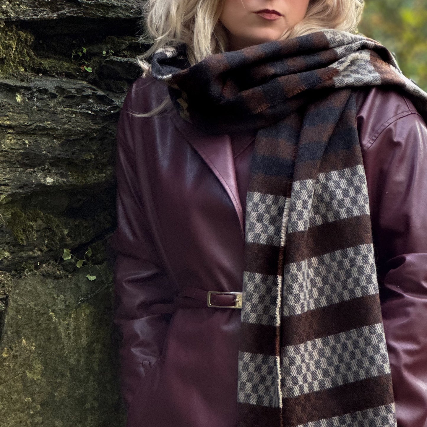 Person wearing a plaid scarf and purple coat against a stone wall.
