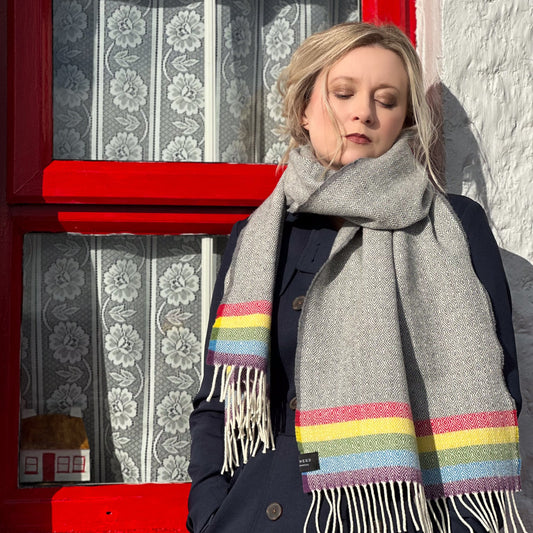 Person wearing a gray scarf with colorful stripes in front of a red door.
