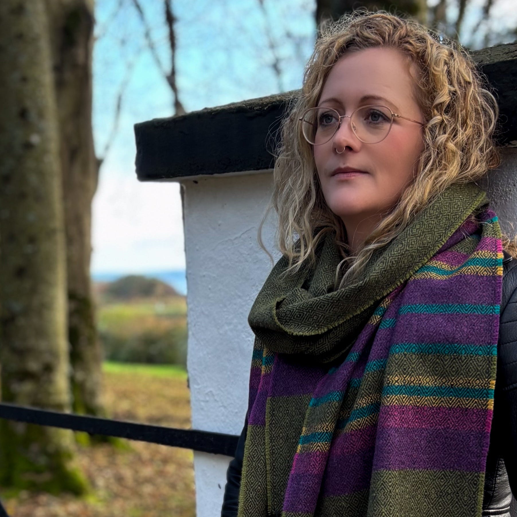 Woman wearing a colorful scarf and glasses outdoors with trees and a building in the background