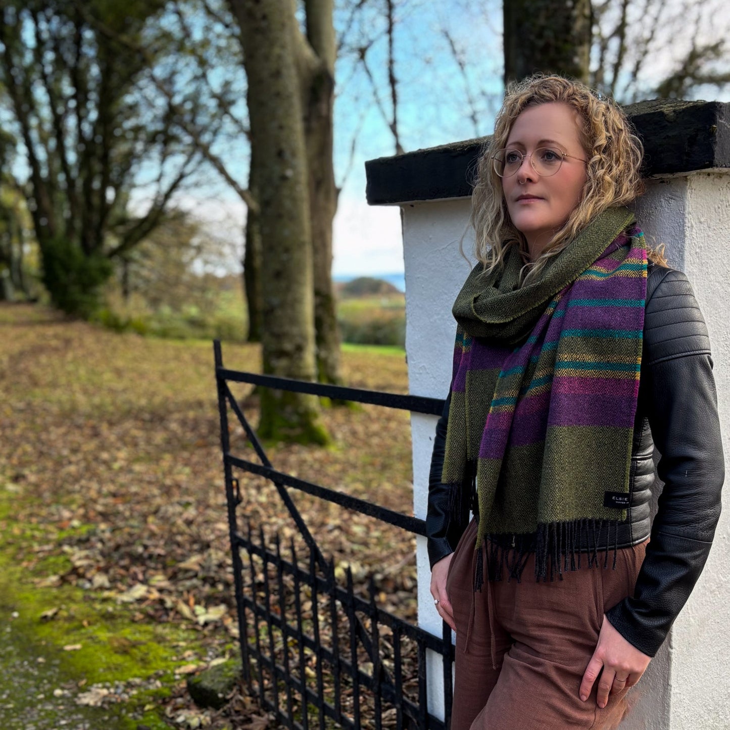 Woman standing outdoors near a gate with trees and grass in the background