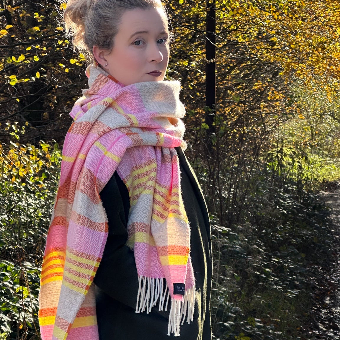 Person wearing a pink and yellow plaid scarf outdoors with trees in the background