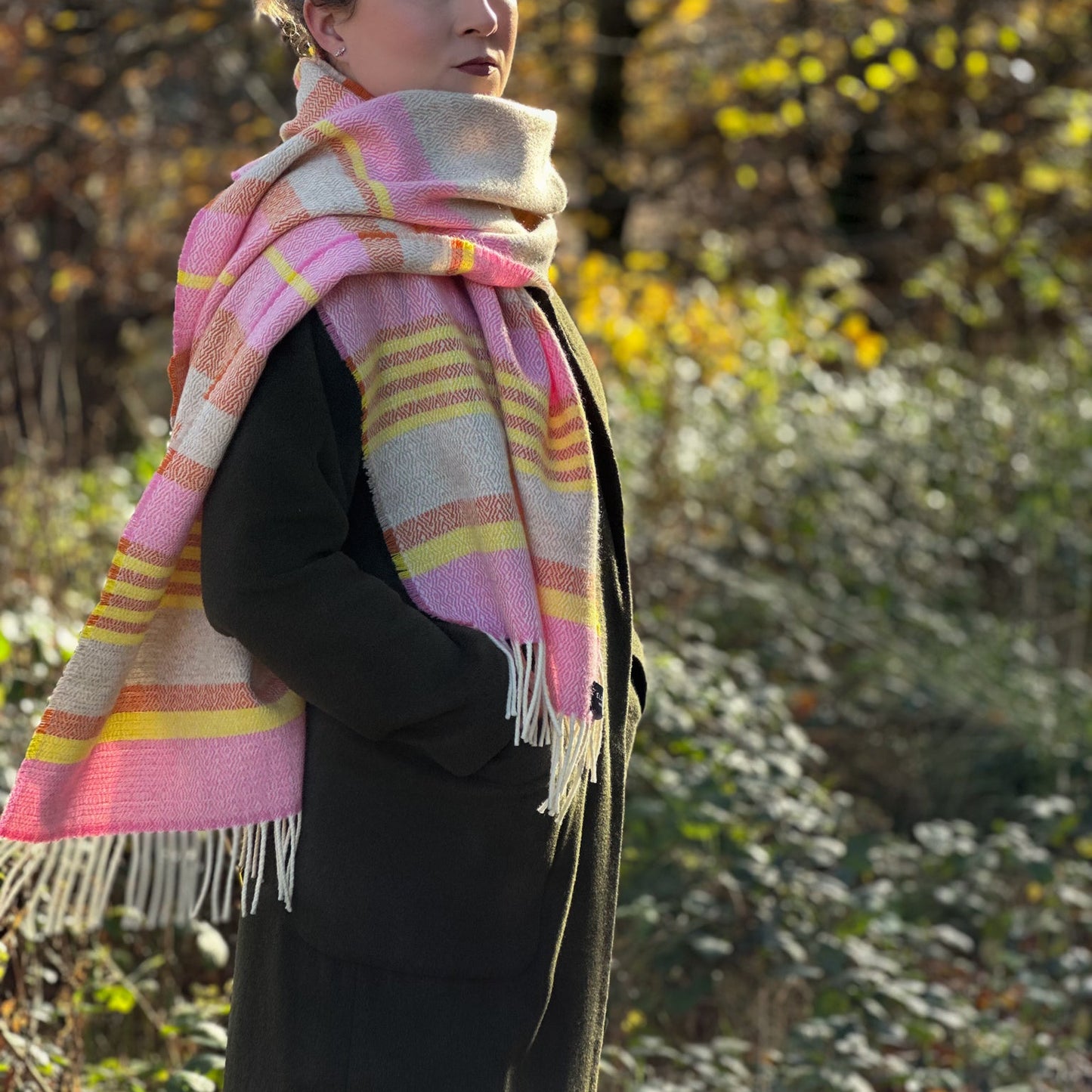 Woman wearing a pink and yellow plaid scarf in a natural setting with trees and bushes.