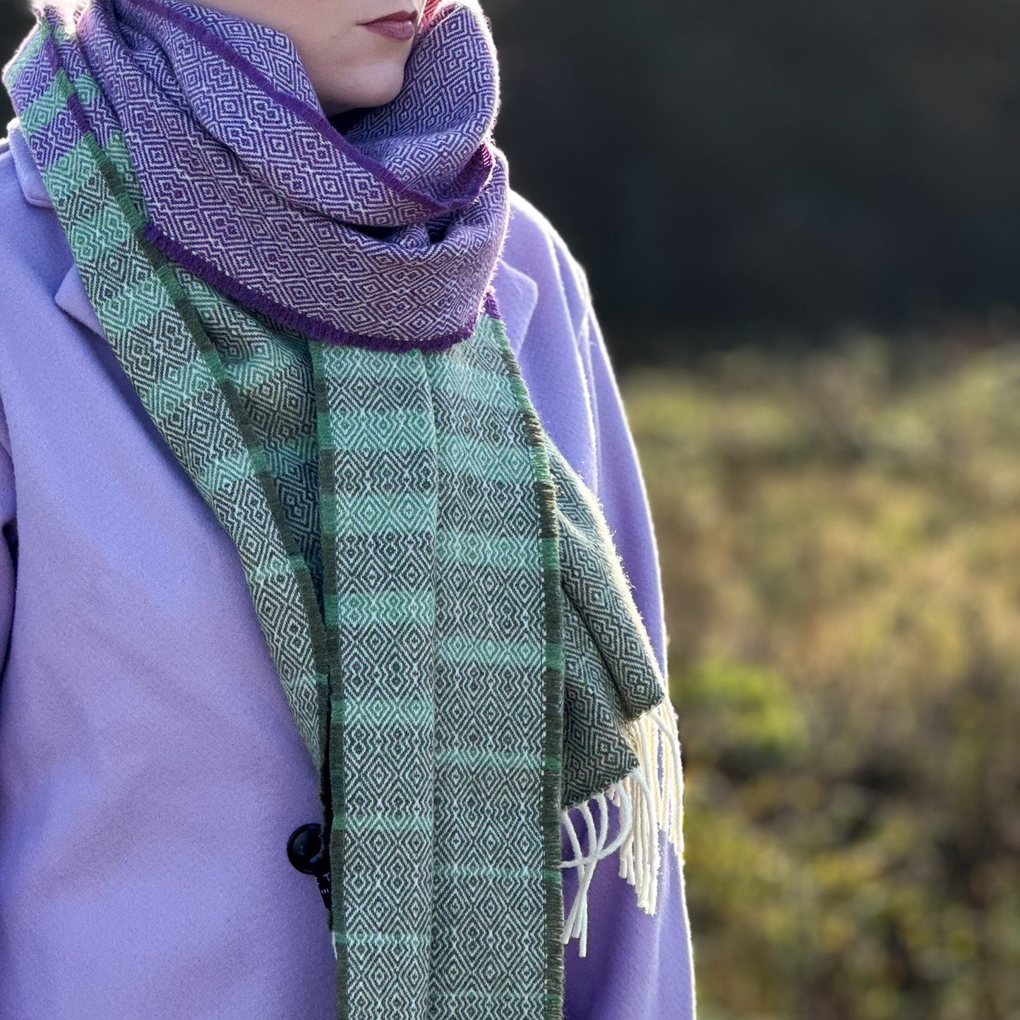 Person wearing a green and purple scarf with a blurred natural background