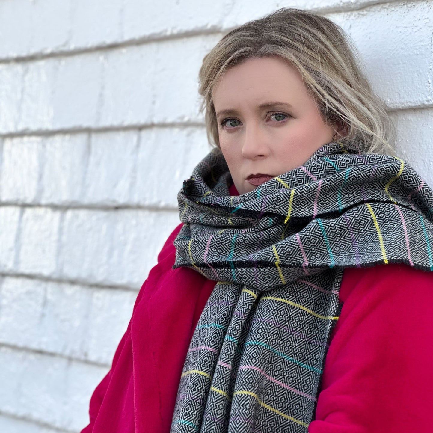 Woman wearing a plaid scarf and pink coat against a white wall.