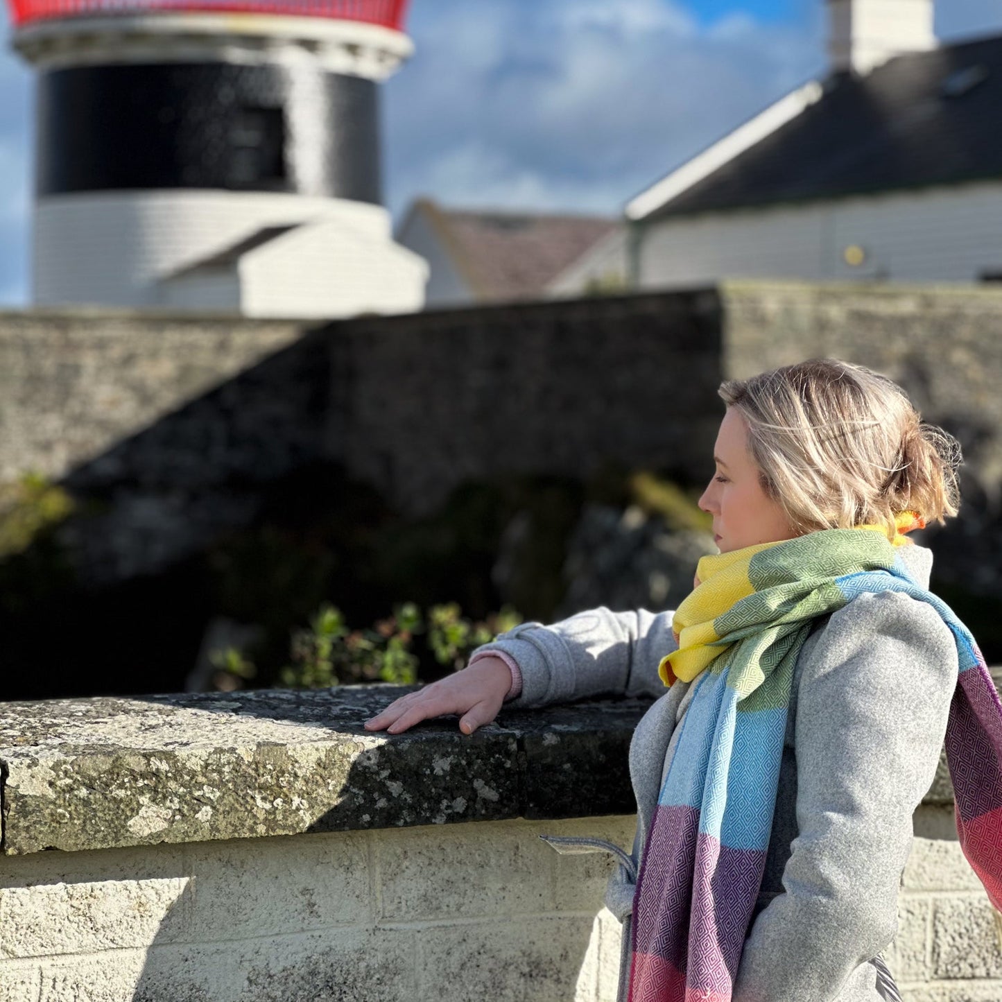 Woman wearing a colorful rainbow scarf standing in front of a lighthouse.