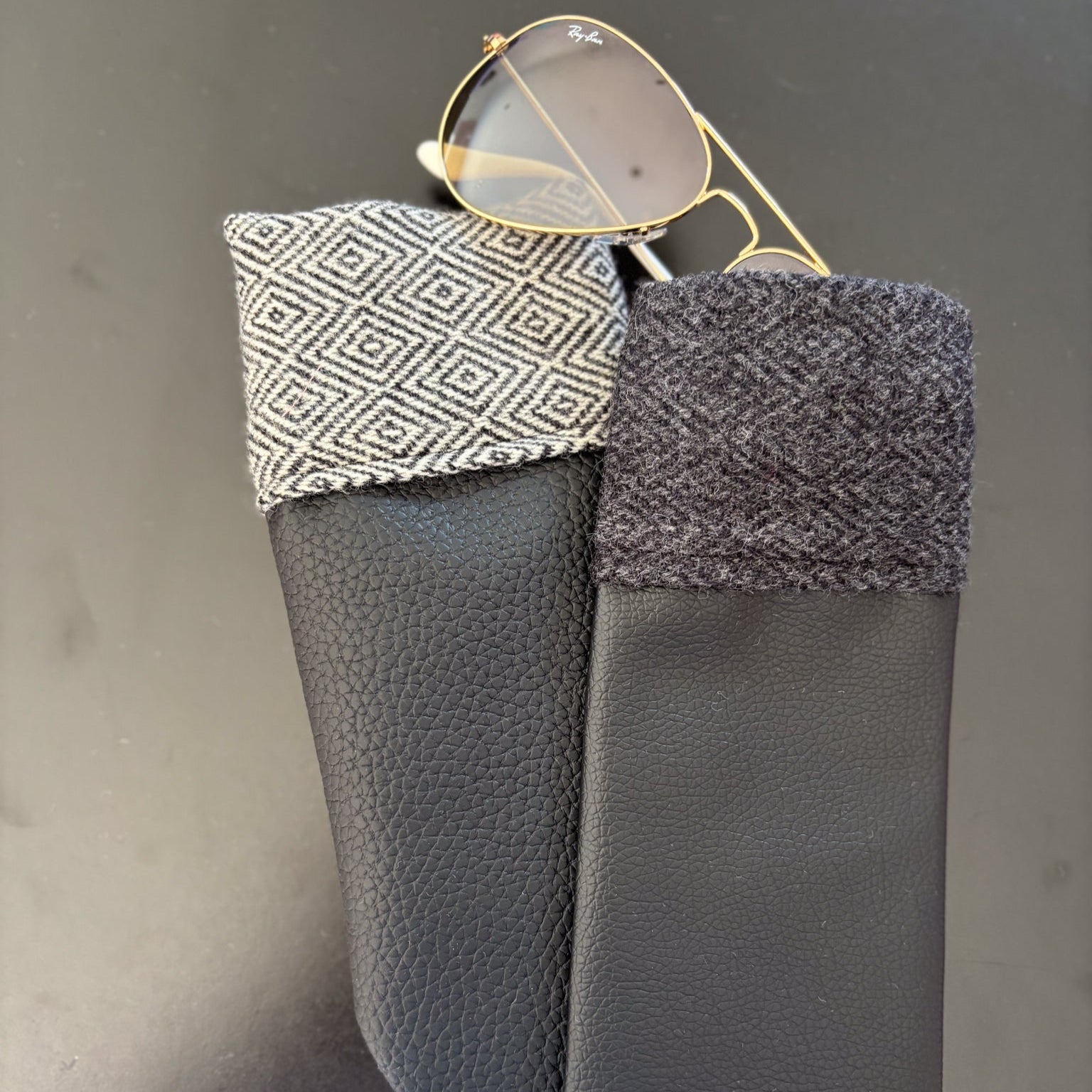 Black leather sunglasses case with patterned flap on a gray background