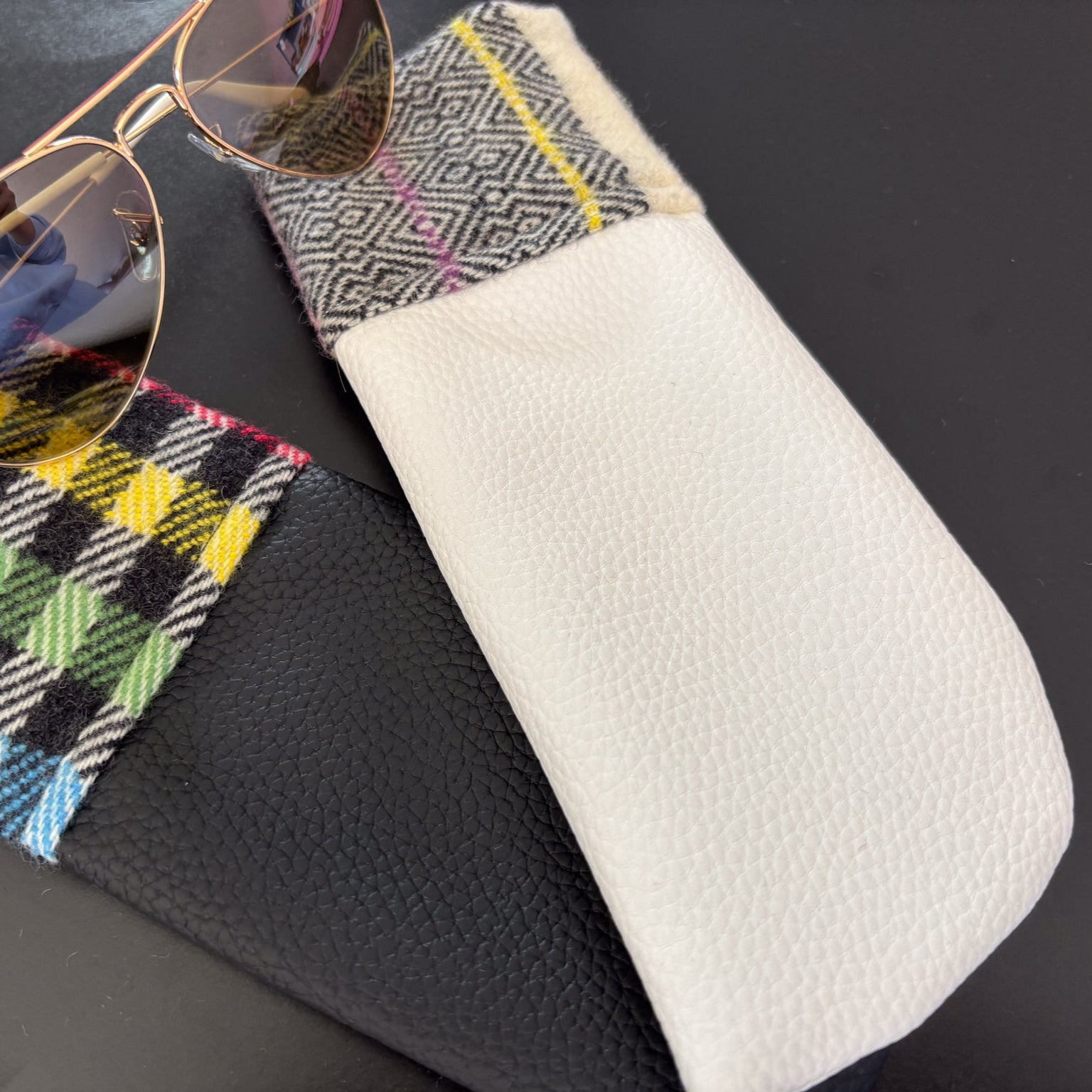 Sunglasses on a patterned case with a white pouch on a black background