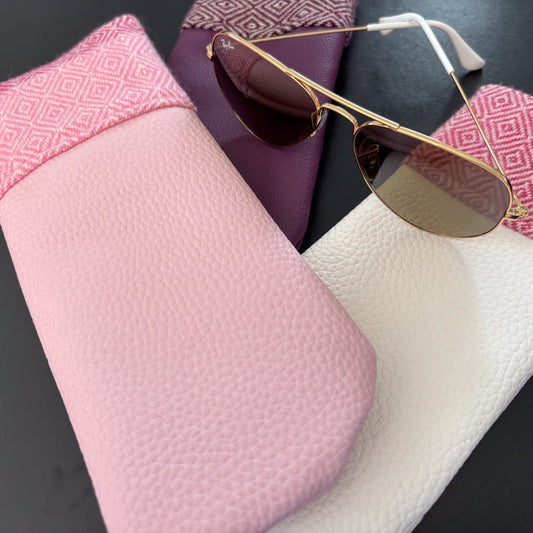Pink sunglasses case with gold-framed sunglasses on a dark surface