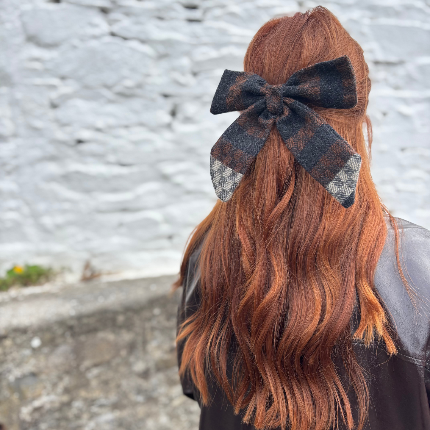 Person with long wavy hair wearing a Tweed bow tie against a textured wall background
