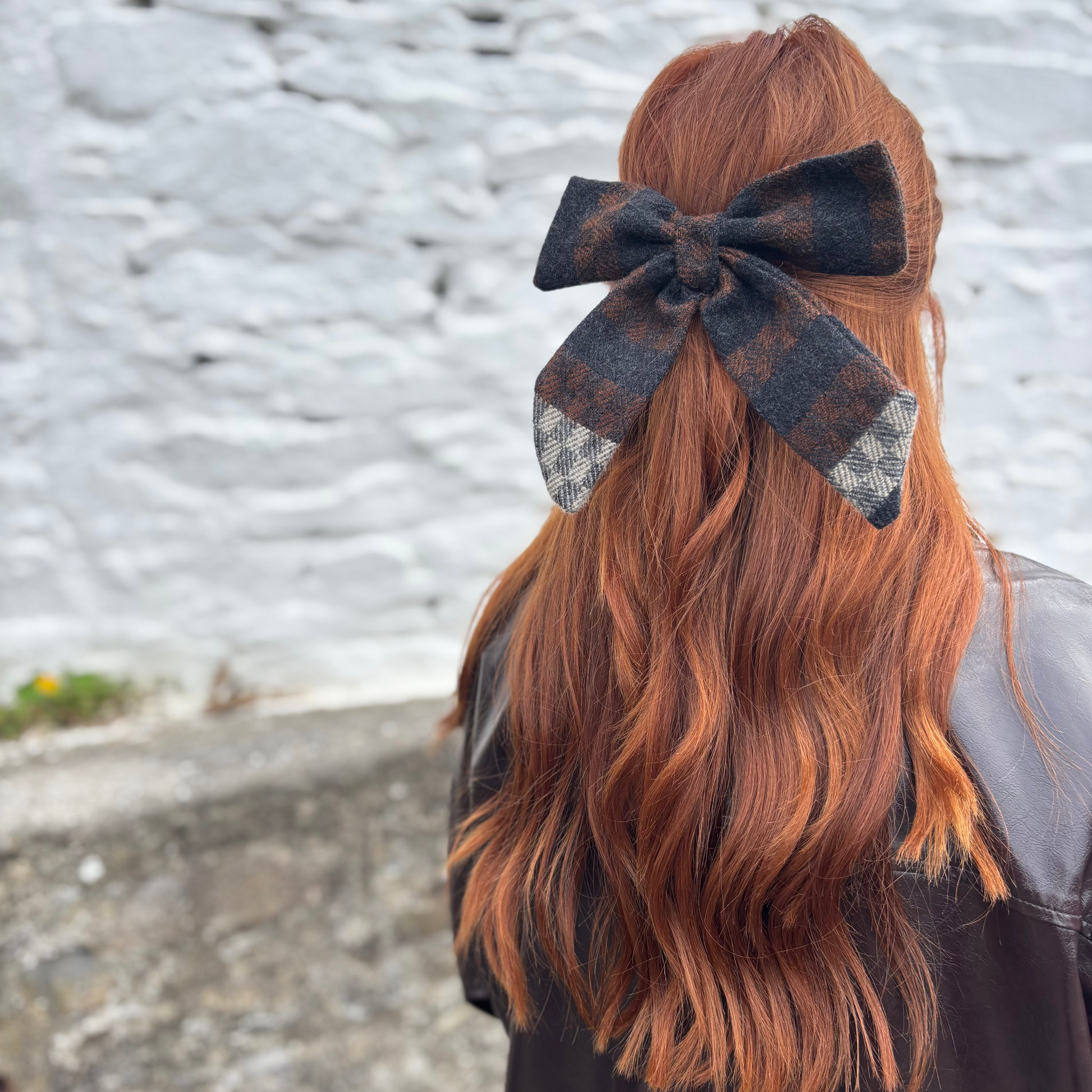 Person with long wavy hair wearing a Tweed bow tie against a textured wall background