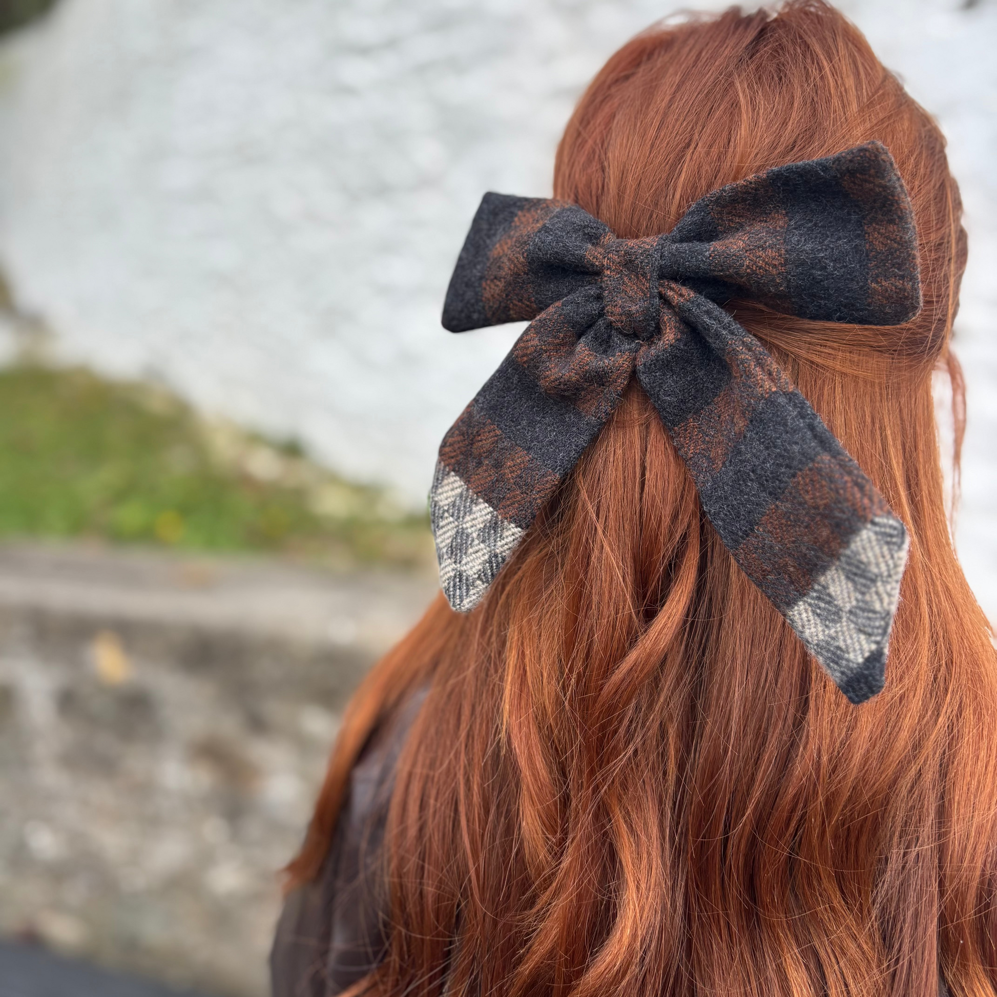 Person with red hair wearing a large black and Tweed bow in their hair, blurred background