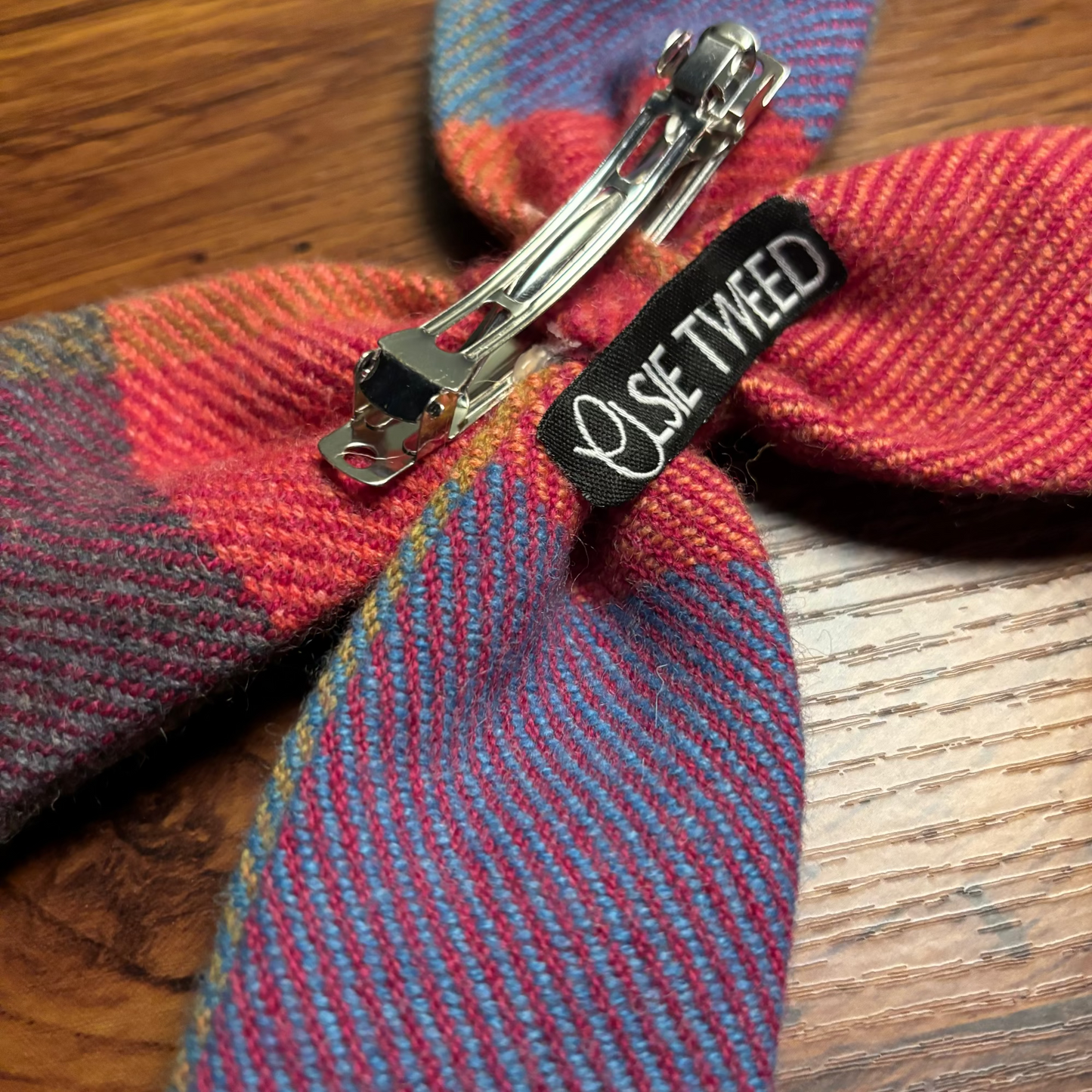 Colorful tweed fabric with a metal clip and 'Ollie Tweed' label on a wooden surface