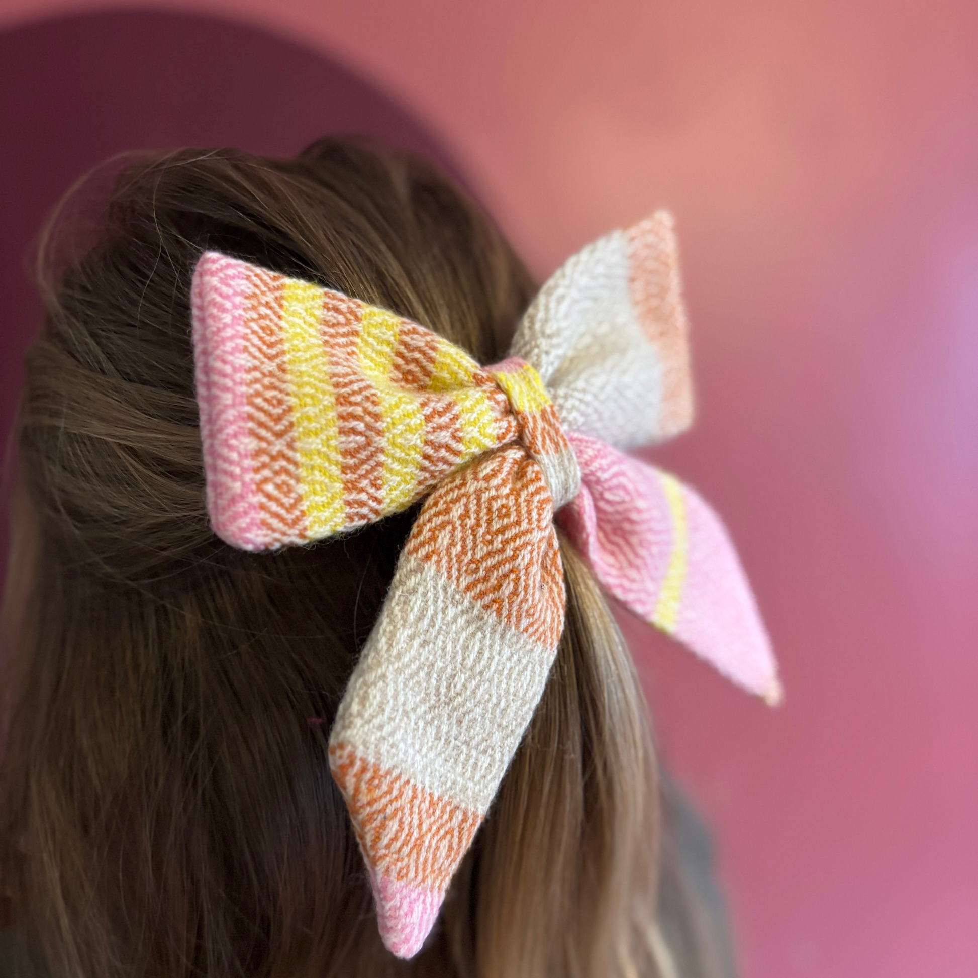 Colorful Tweed hair bow on a person's head with a pink background