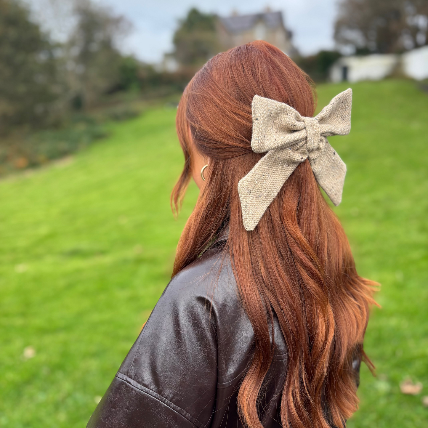 Person with long red hair wearing a beige tweed bow in a park