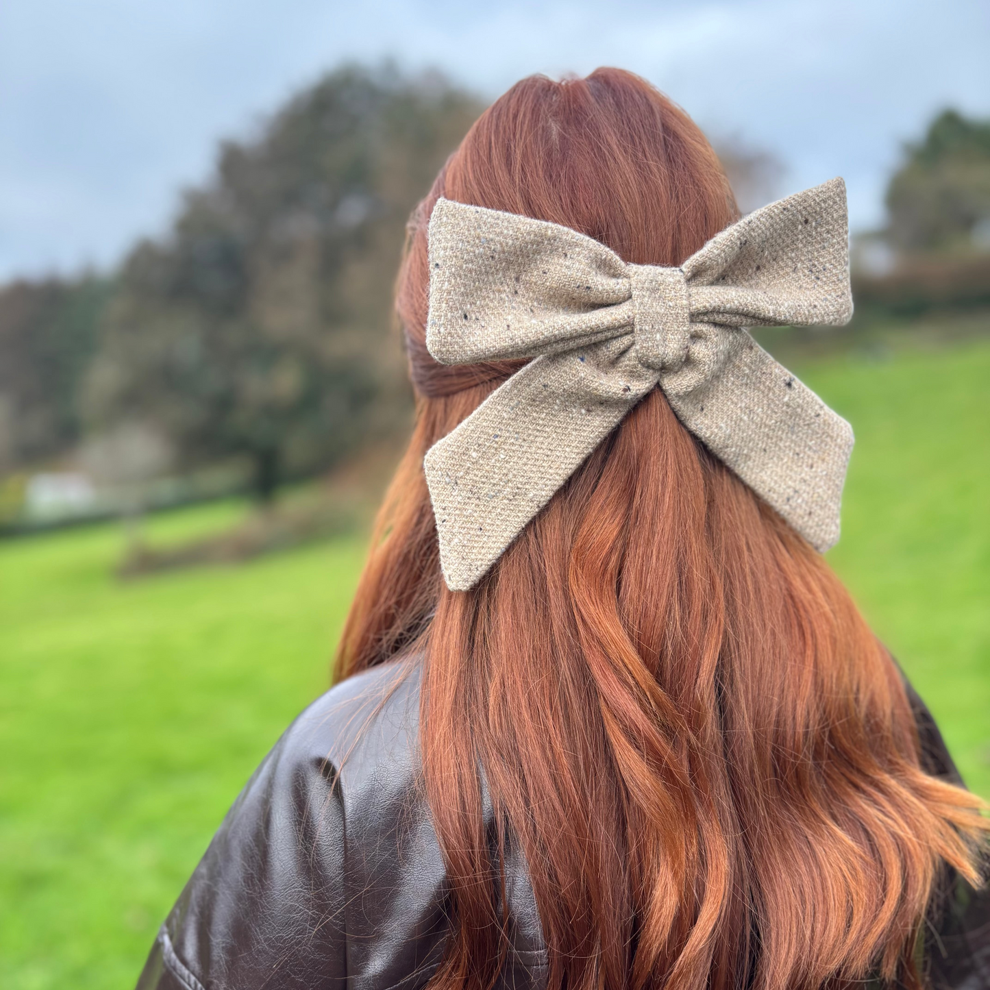 Person with red hair wearing a beige tweed bow, standing in a grassy field.