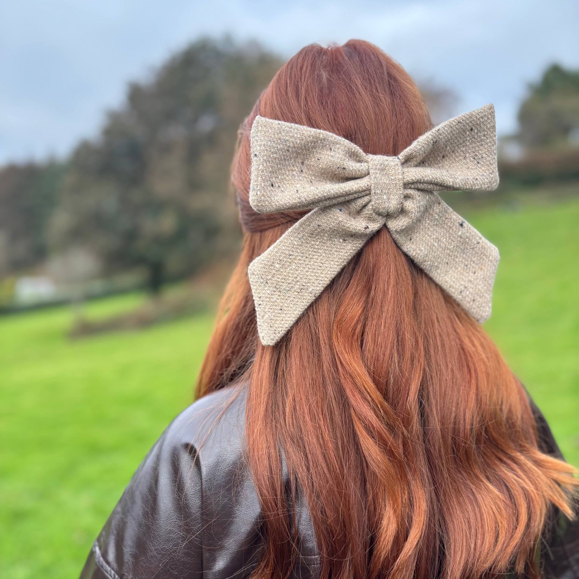 Person with red hair wearing a beige tweed bow, standing in a grassy field.