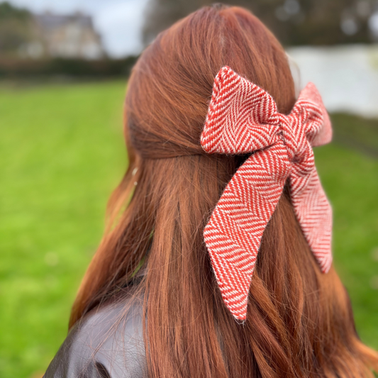 Person with red hair wearing a orange tweed and white checkered hair bow outdoors.