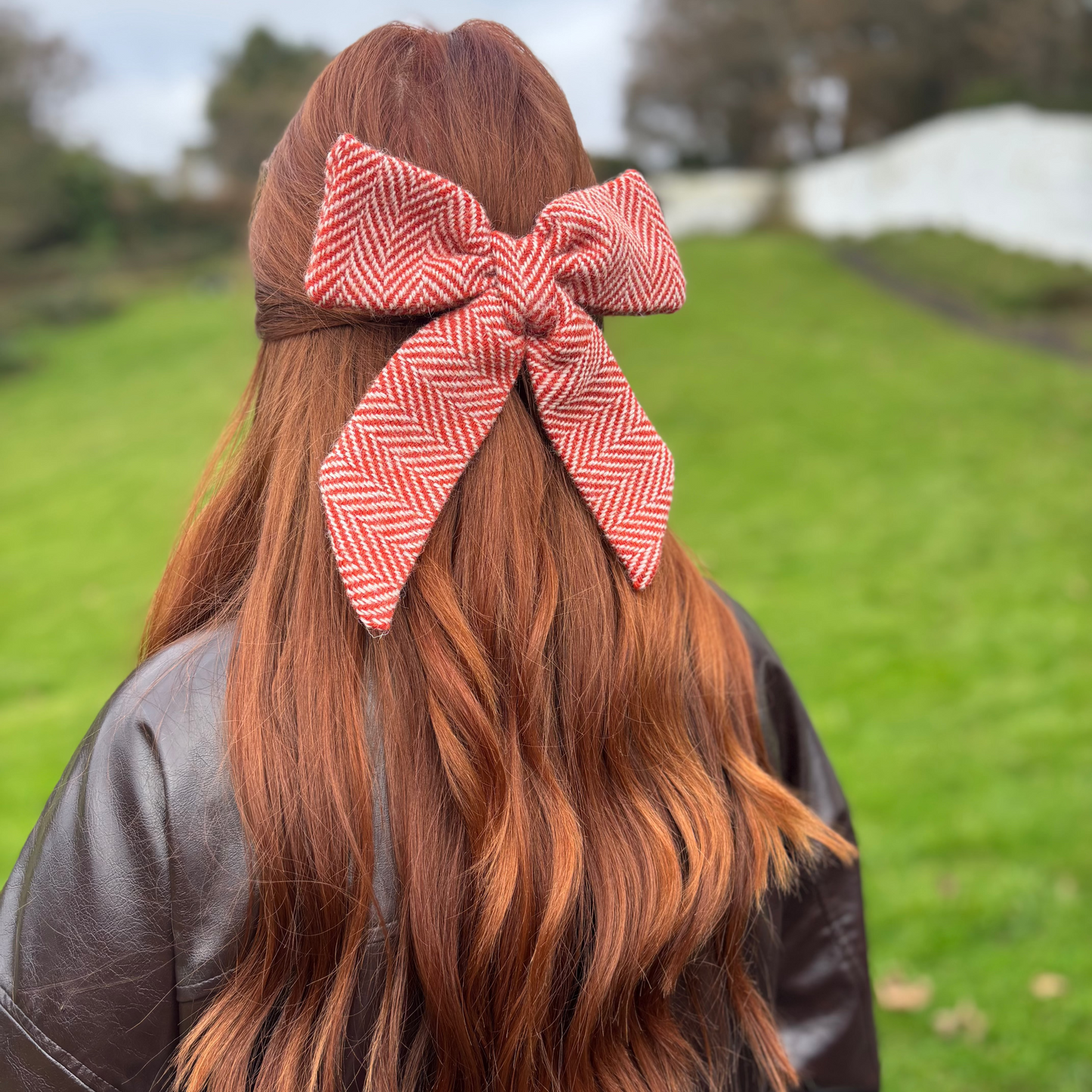 Person with red hair tied with a large red and white checkered bow outdoors.