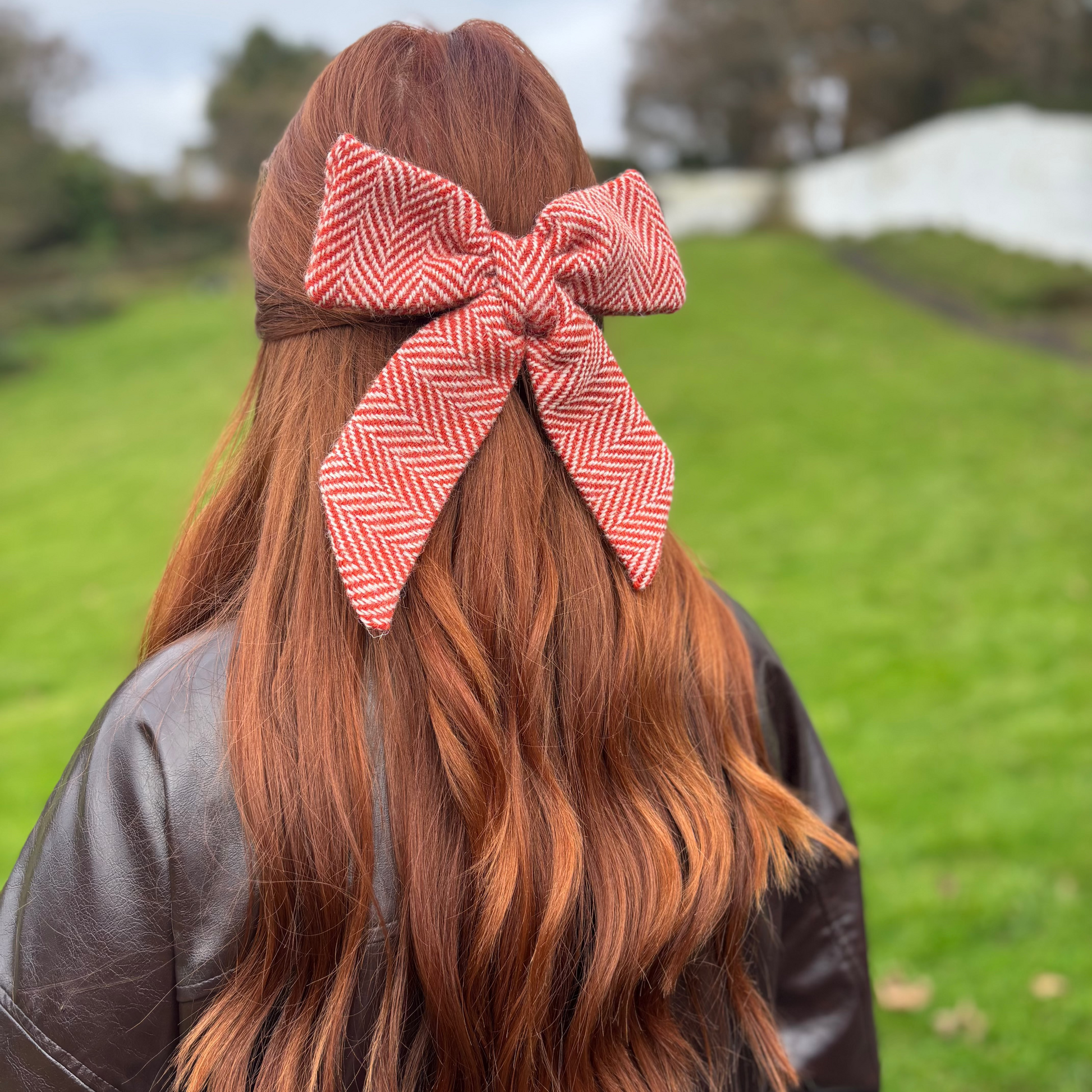 Person with red hair tied with a large red and white checkered bow outdoors.