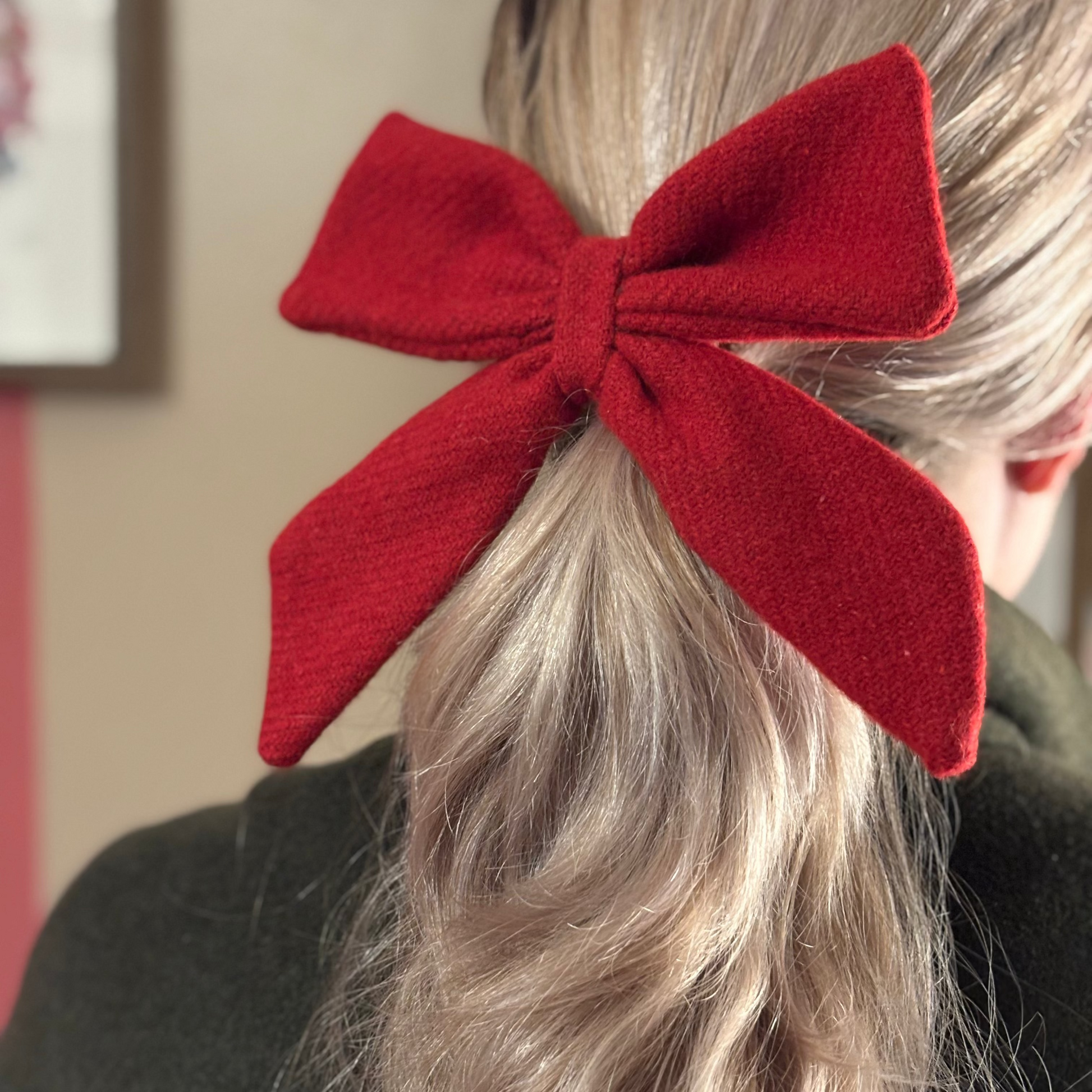 Person wearing a large red tweed bow in their hair with a neutral background