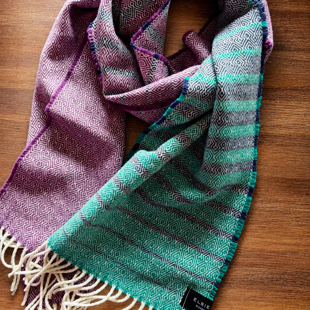 Woven scarf with purple and green patterns on a wooden surface