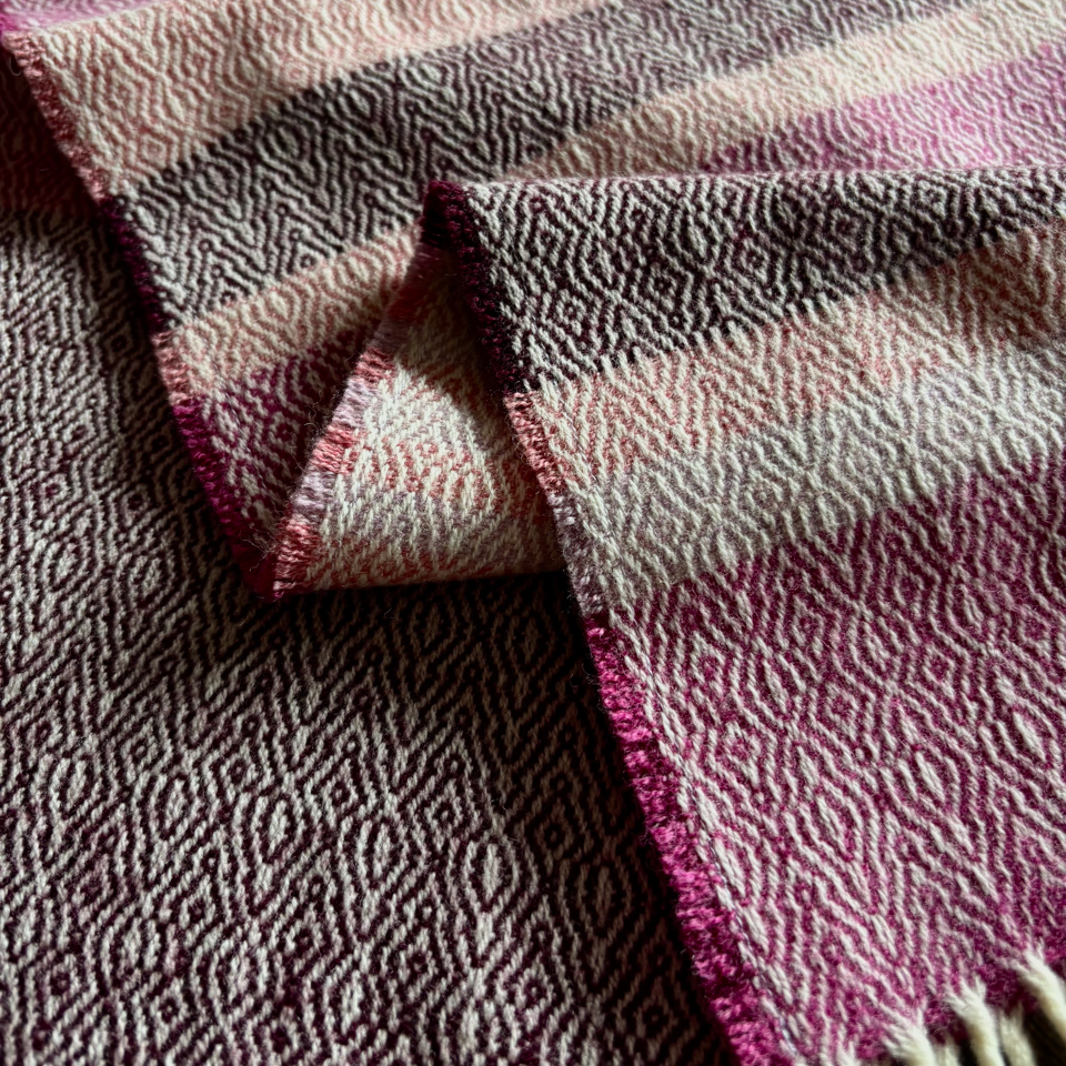 Close-up of a textured donegal tweed fabric with pink and plum and pink stripes on a dark surface
