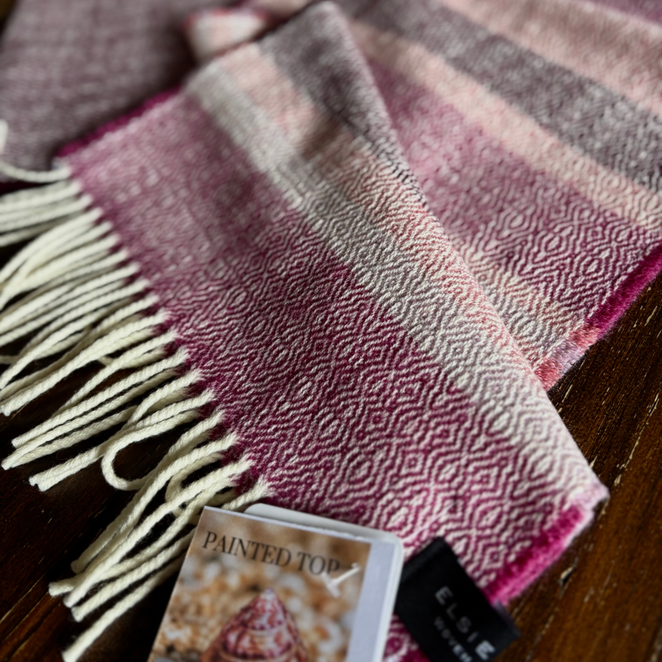 Plaid scarf with fringes on a wooden surface, featuring a 'Painted Top shell' tag.
